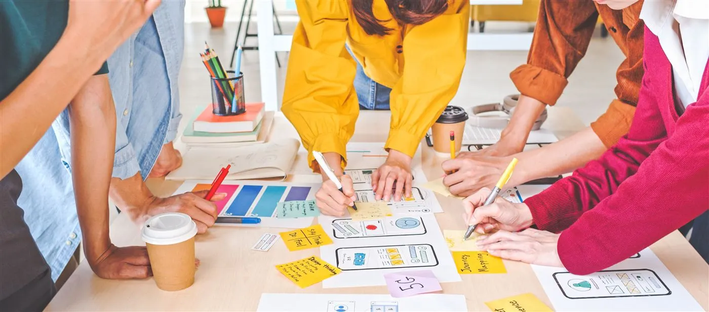 Designers sketching mobile app wireframes around a table