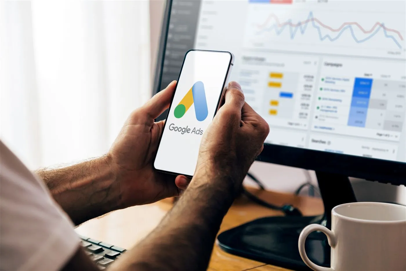 The Google Ads app opening on a phone in front of a campaign dashboard