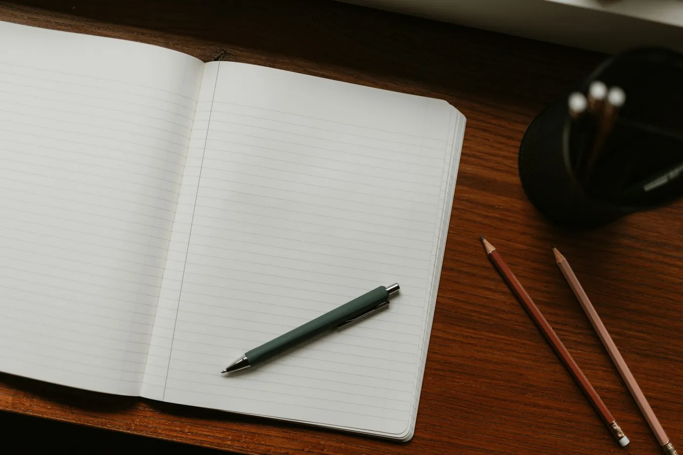 An open notebook with pen and pencils on a wooden desk